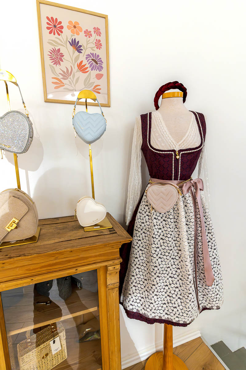 Das Dirndl „Amy“ mit der ikonischen Spitzenschürze im Blümchenmuster wird durch liebevoll ausgewählte Accessoires perfekt ergänzt.