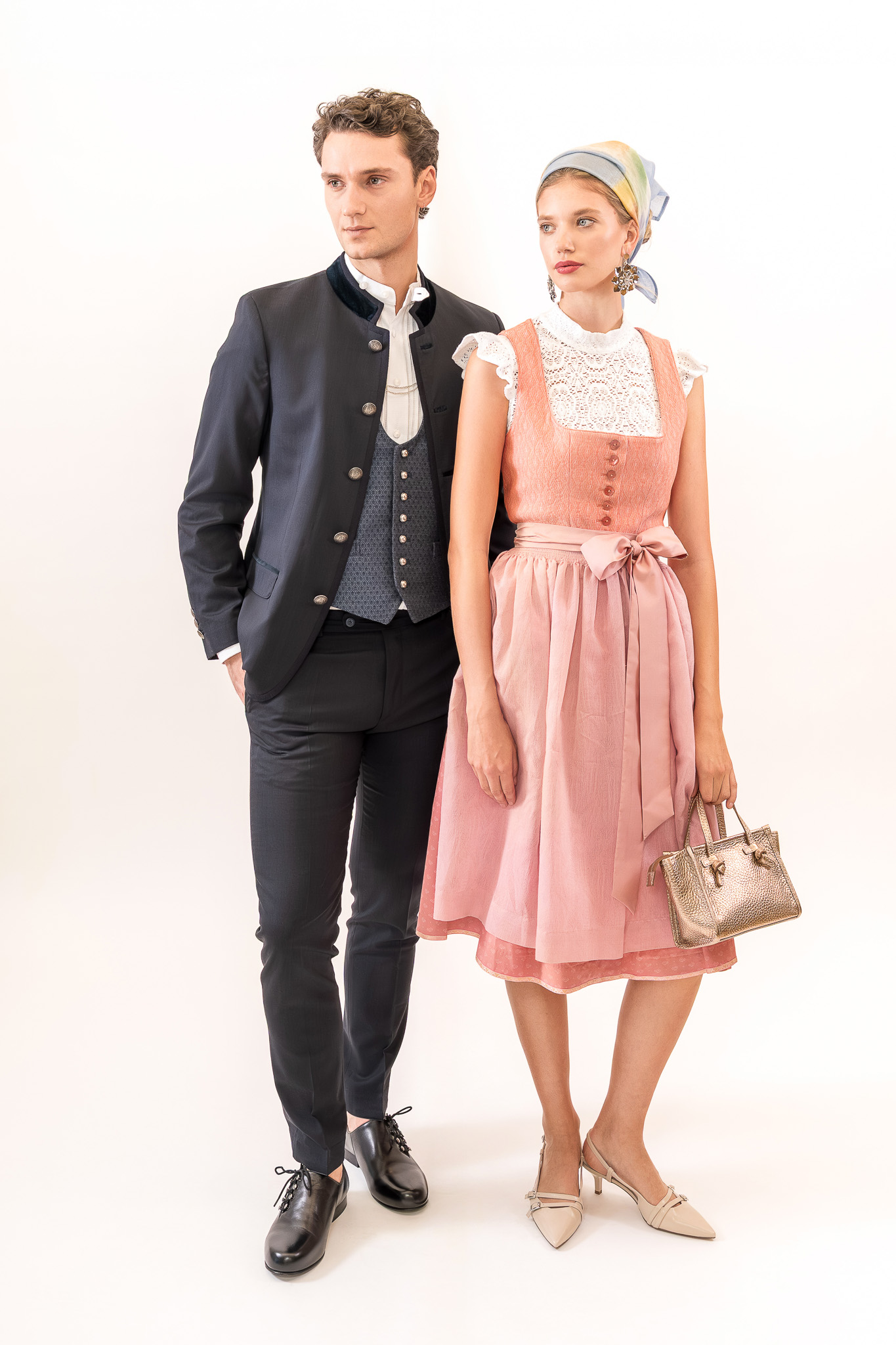dirndl-trends-2026-rose-dirndl-stehkragensakko Modernes Dirndl in Rosé mit Spitzenbluse und Schürze sowie Herrenlook mit dunklem Stehkragensakko – Tracht Frühjahr Sommer 2026.