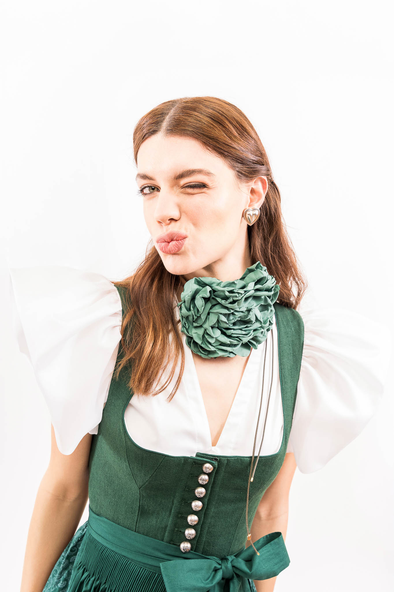 Modernes Dirndl mit Volumenbluse und Statement-Schmuck Grünes Dirndl mit voluminöser Bluse und floralem Halsschmuck – Dirndl Trends Frühjahr Sommer 2026.