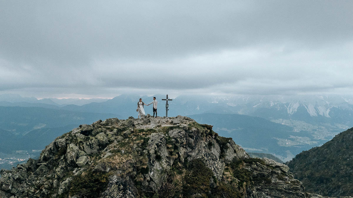Brautpaar steht auf einem Berggipfel neben einem Kreuz