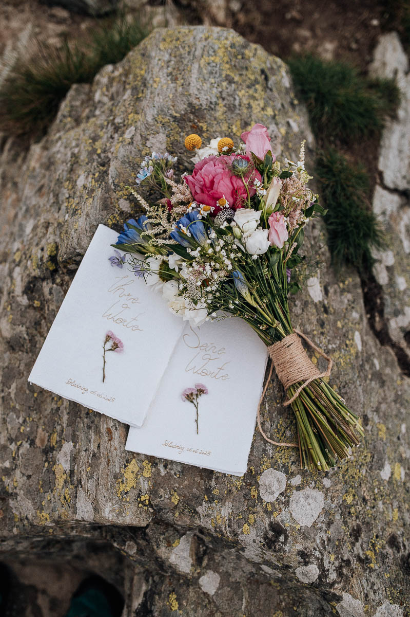 Brautstrauß liegt auf einem Stein neben Hochzeitskarten