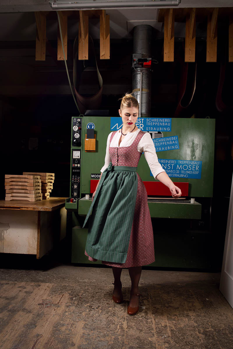Dirndl von Fuchsdeifeswuid in Rot und Grün in einer Werkstatt mit industrieller Maschine
