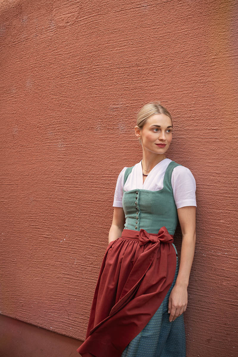 Modernes Dirndl von Fuchsdeifeswuid mit roter Schürze vor einer farbigen Wand
