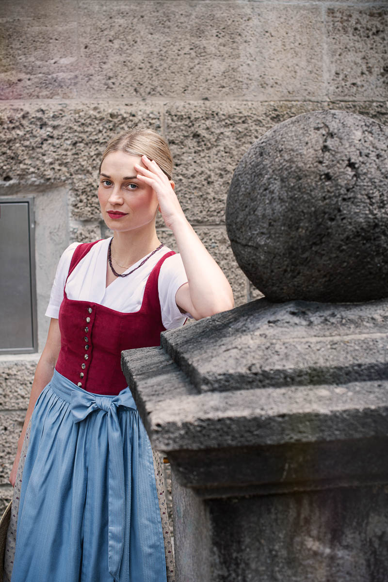 Dirndl von Fuchsdeifeswuid in Weinrot und Blau in einer städtischen Umgebung mit Steinarchitektur