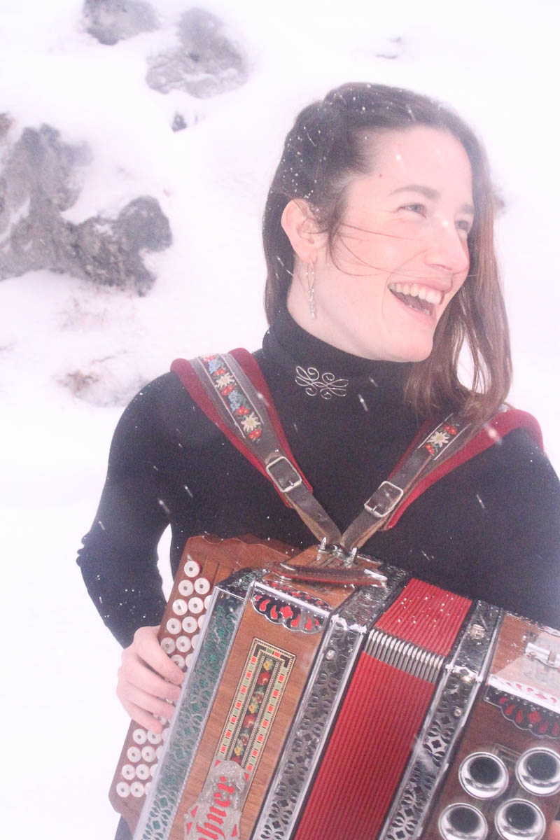 Frau mit Akkordeon steht lachend im Schnee und trägt ein Outfit von MARIAHAUSE