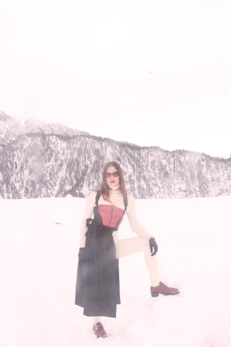 Frau in vollständigem MARIAHAUSE Outfit steht im Schnee mit Bergen im Hintergrund