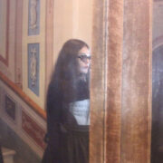Frau mit Sonnenbrille trägt ein Korsett von MARIAHAUSE und steht vor einem Spiegel in einem historischen Interieur