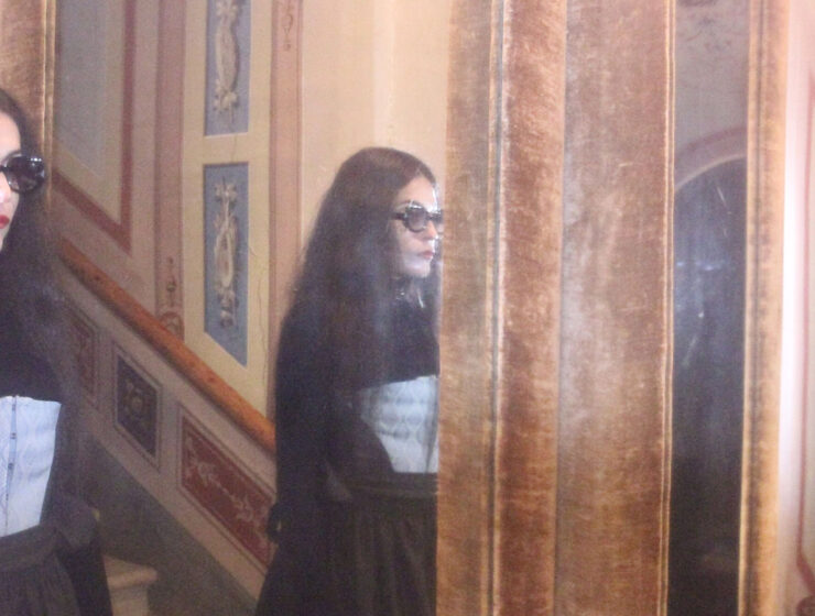 Frau mit Sonnenbrille trägt ein Korsett von MARIAHAUSE und steht vor einem Spiegel in einem historischen Interieur