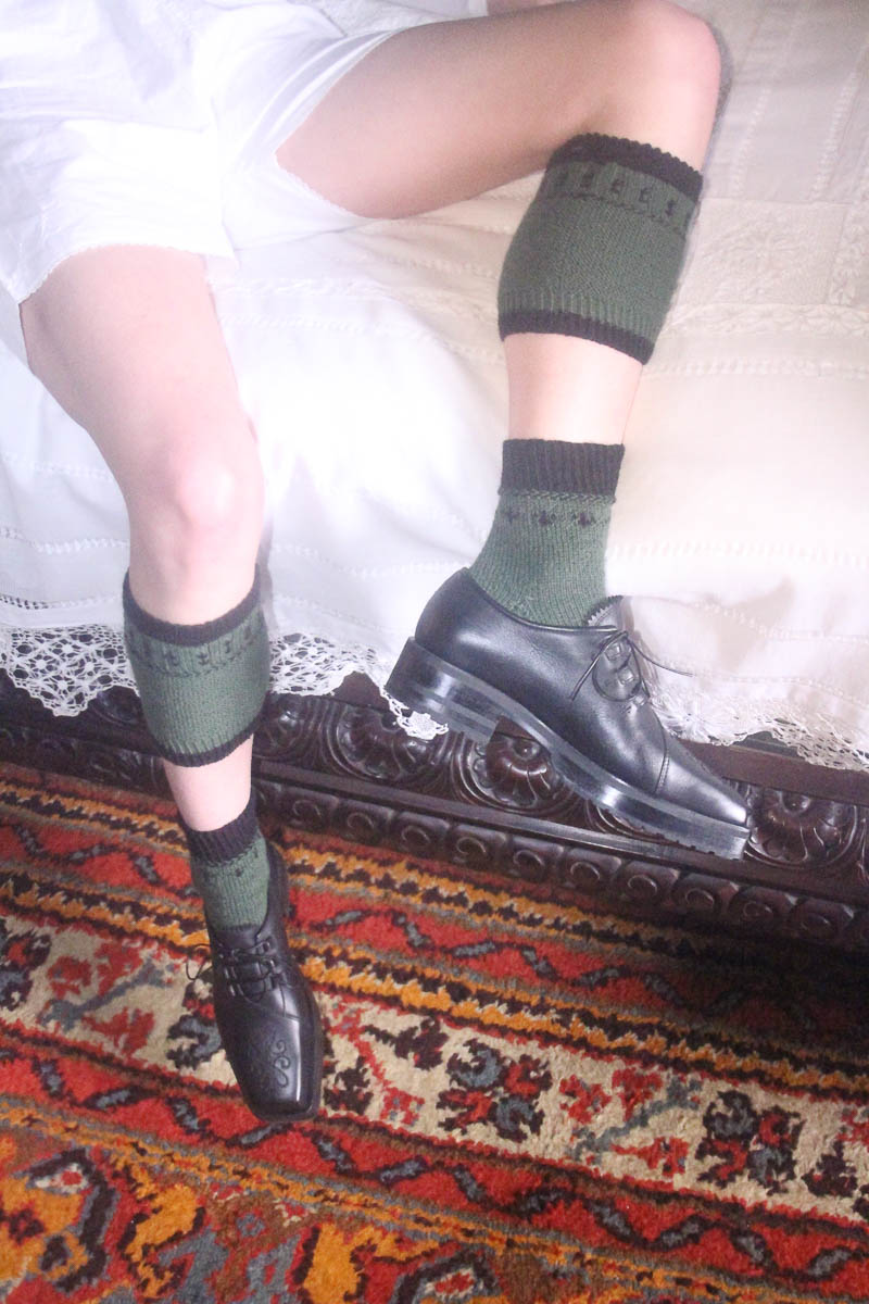 Grüne gestrickte Socken und schwarze Lederschuhe von MARIAHAUSE auf gemustertem Teppich