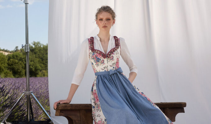 Frau im floralen Dirndl mit blauer Schürze vor hellem Hintergrund und Lavendelfeld – Muttertag 2026 Mode Inspiration
