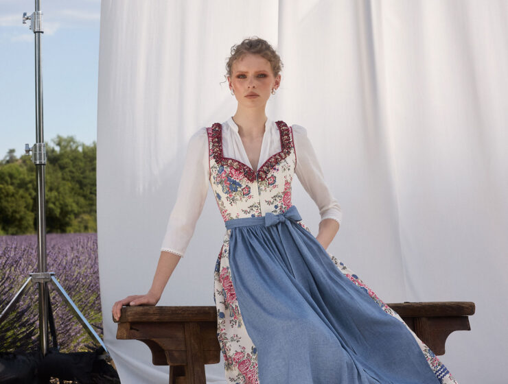 Frau im floralen Dirndl mit blauer Schürze vor hellem Hintergrund und Lavendelfeld – Muttertag 2026 Mode Inspiration