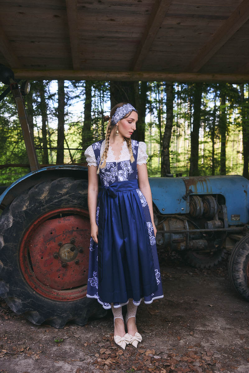 Moderne Tracht mit Vintage-Flair Model im blauen Dirndl neben einem alten Traktor