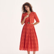 Model trägt ein korallrotes Spitzenkleid mit passender Jacke im Color-Blocking-Trend 2026 vor hellem Studiohintergrund.