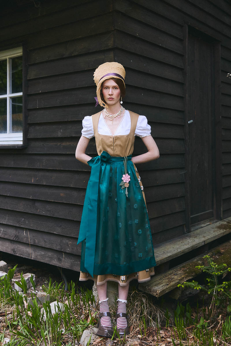 Moderne alpine Romantik Model in grünem Dirndl vor dunklem Holzhaus