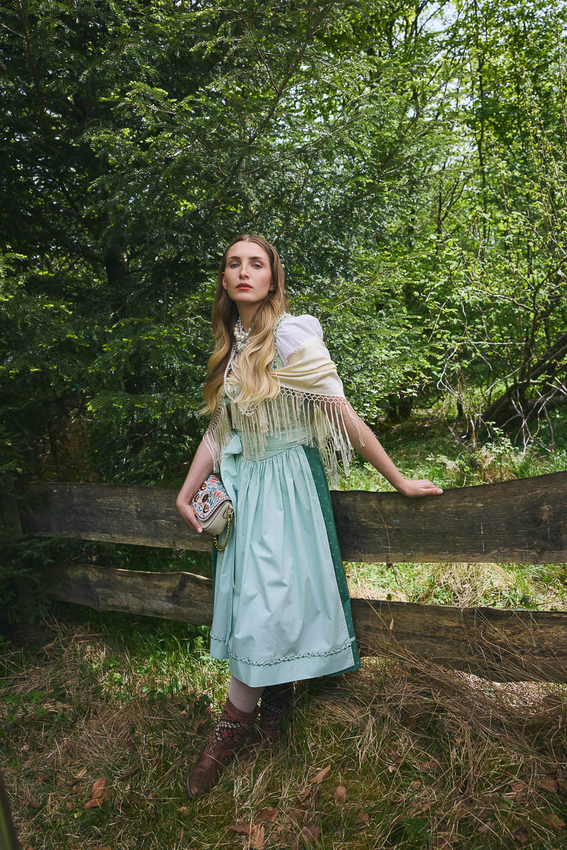 Alpine Cottagecore-Romantik Model im mintgrünen Dirndl mit Fransen und Perlenaccessoires im Wald