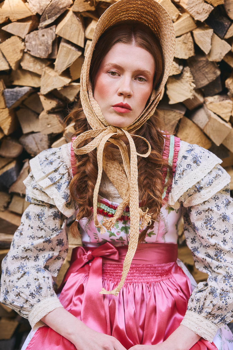 Märchenhafte Trachtenromantik Portrait eines Models im rosa Dirndl mit Strohhut vor Holzstapeln