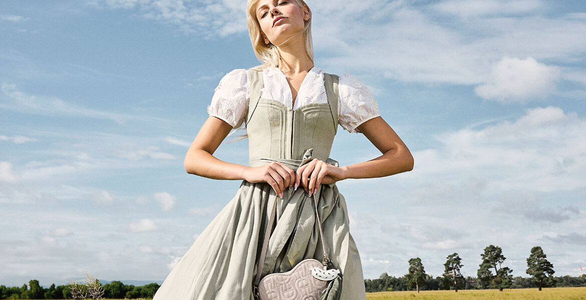 Modernes grünes Dirndl in Salbei von CocoVero aus der Frühjahr/Sommer-Kollektion 2026 auf einer sommerlichen Wiese fotografiert