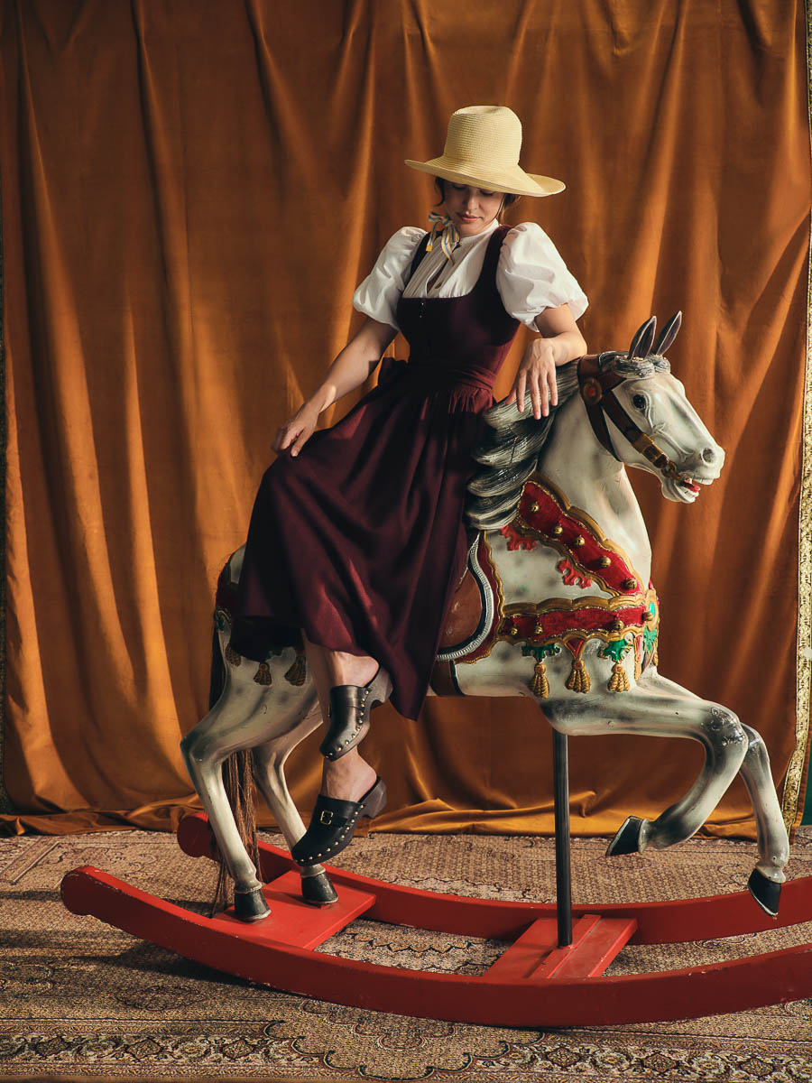 Dirndl Monika von Gottseidank rau im bordeauxroten Dirndl Monika von Gottseidank auf einem historischen Schaukelpferd