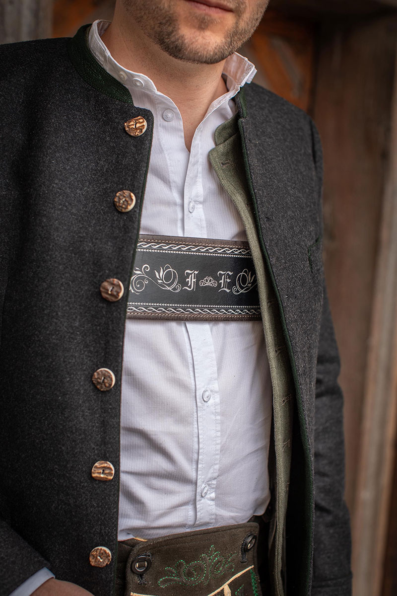 Mann trägt einen verzierten Lederhosenträger zu weißem Hemd und dunkler Trachtenweste
