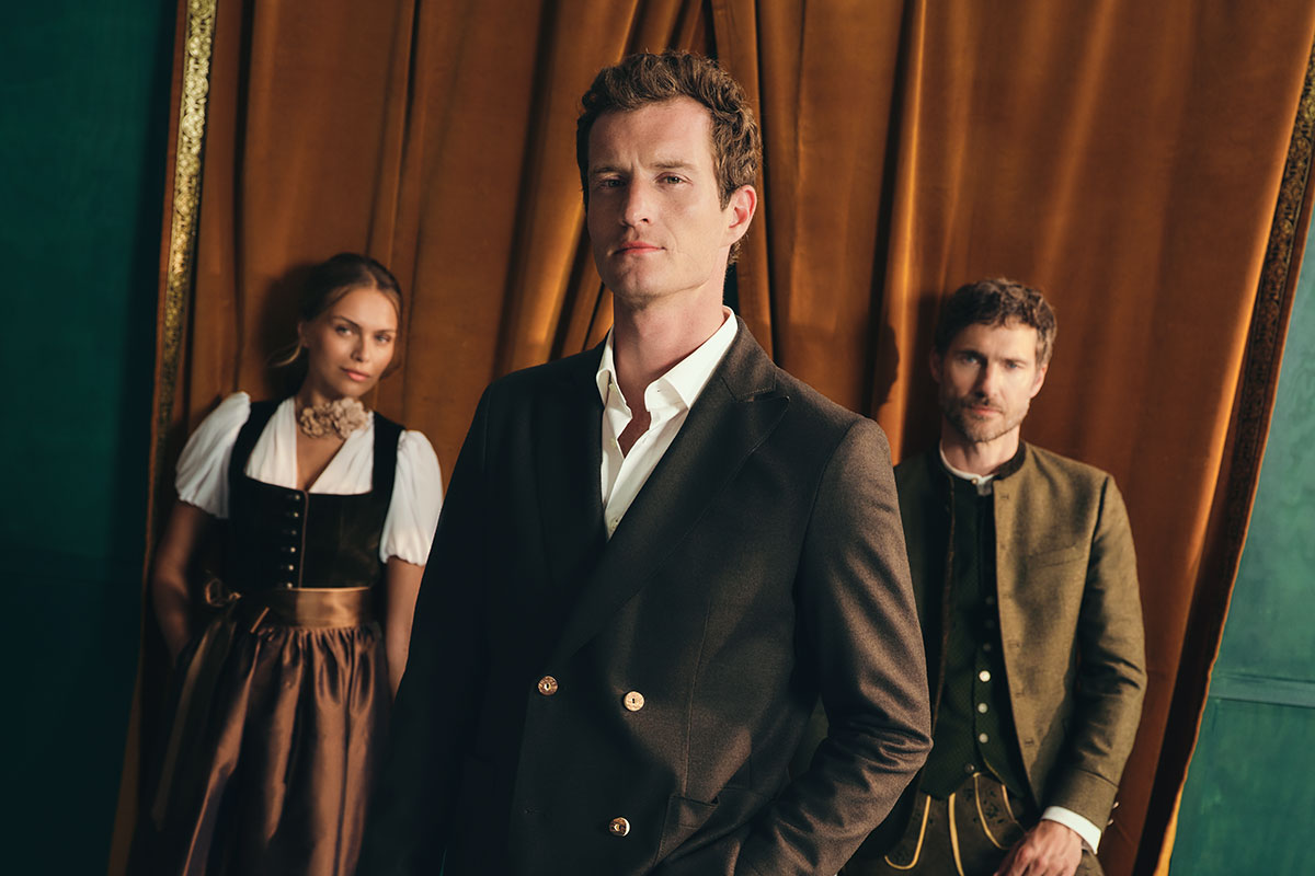 Drei Models in moderner Tracht von HIRMER, im Vordergrund ein Mann im dunklen Trachtenanzug