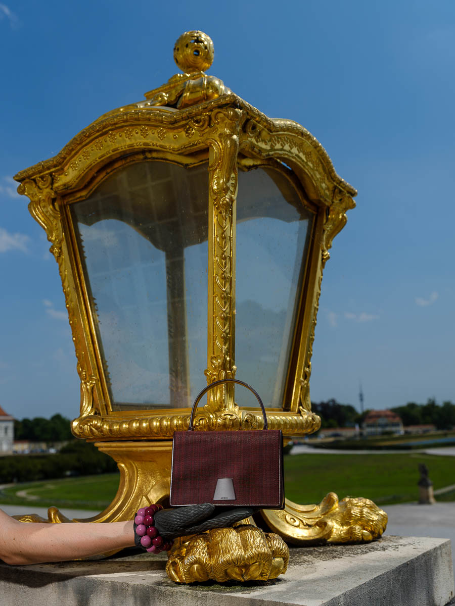 Akris-Handtasche mit schwarzen Lederhandschuhen vor einer goldenen Laterne im Schlosspark Nymphenburg