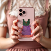 Rosafarbene Handyhülle mit gesticktem Dirndl-Motiv von Mimi’s Glow, gehalten vor einem rosafarbenen Dirndl.