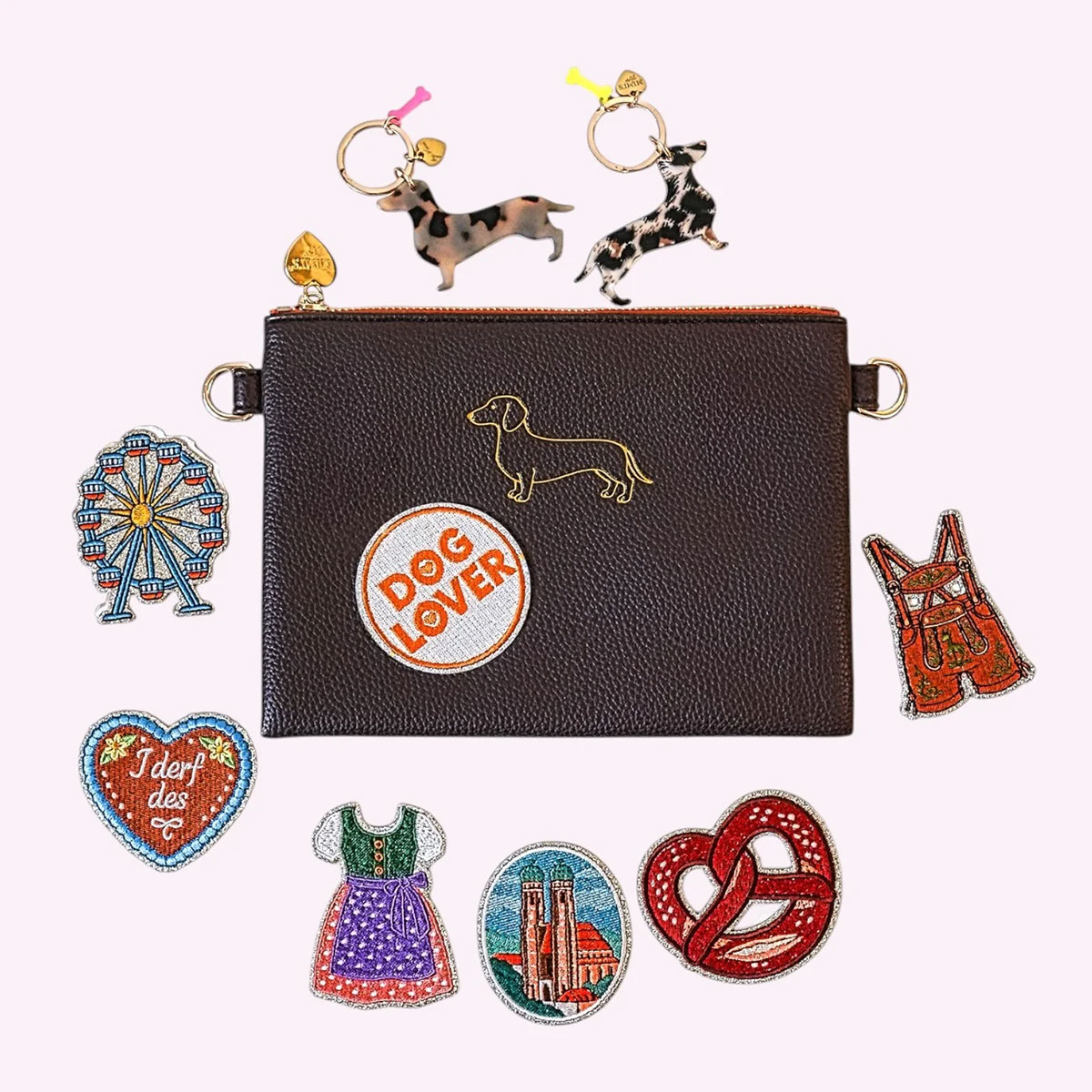 Dunkelbraune Pouch von Mimi’s Glow mit Dackelmotiv und Dog-Lover-Sticker, umgeben von Stickern mit Dirndl, Breze, Riesenrad und München-Motiven sowie Dackelanhängern.
